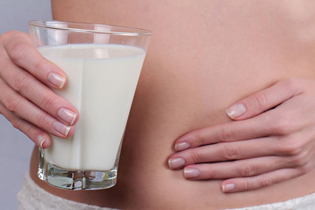 A woman pressing on her stomach while holding a glass of milk