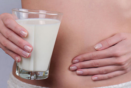 A woman pressing on her stomach while holding a glass of milk