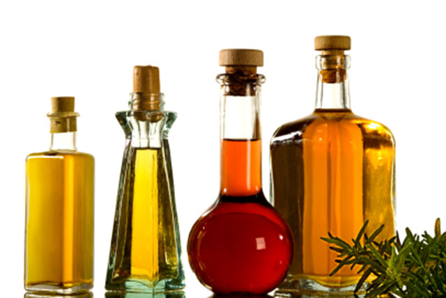 Several oils in glass bottles on a flat surface with a sprig of rosemary